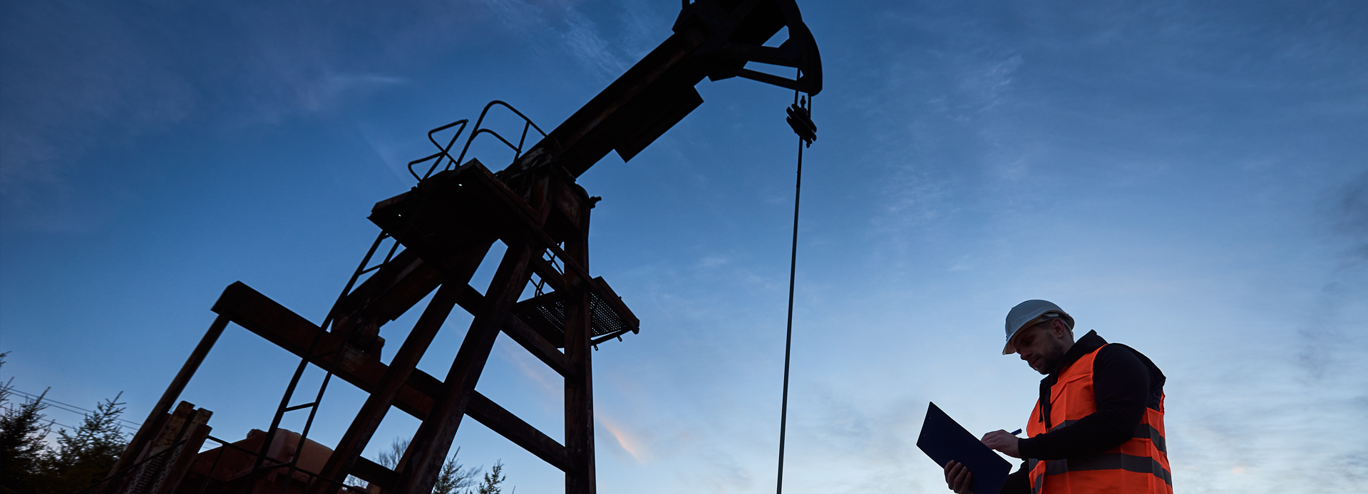 Field technician recording measurement data beside a pumpjack at dusk